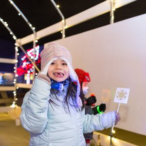 Child holds a snowflake light stencil and smiles at the camera.