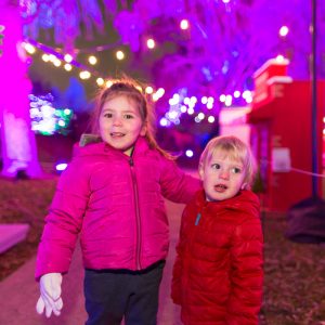 Young girl with her arm around young boy in front of sea of purple light.